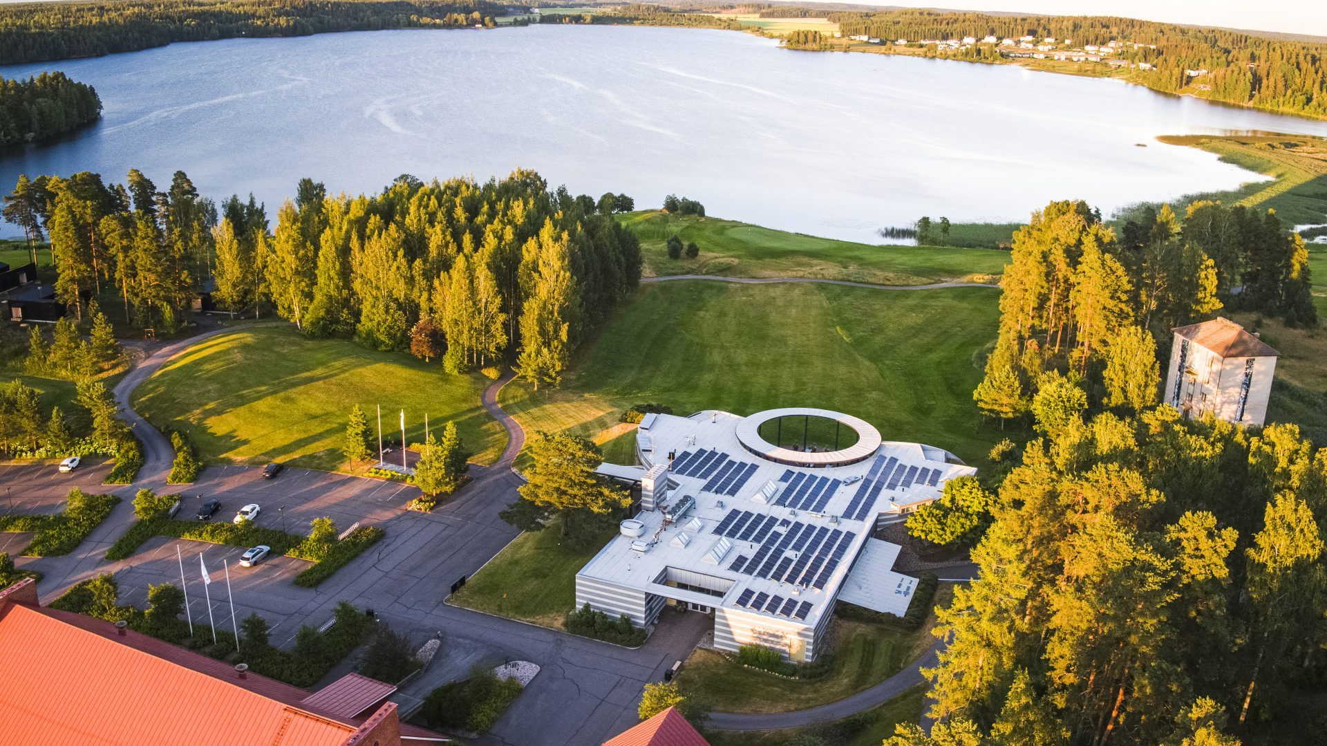 A modern building with solar panels nestled in a lush landscape by a northern Finnish lake.