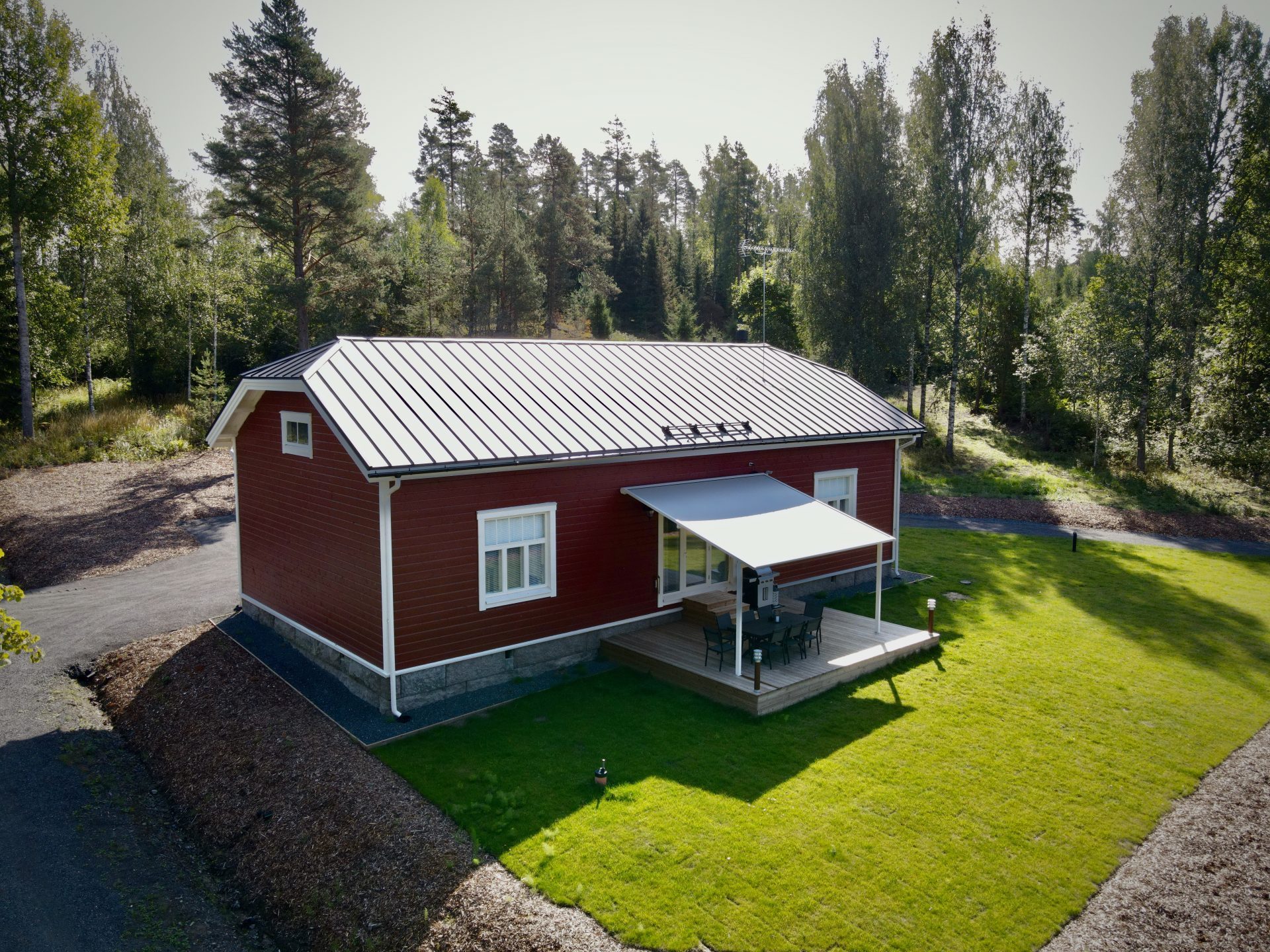 Punainen omakotitalo nurmikkoalueella, jossa on terassi ja pihakalusteet.