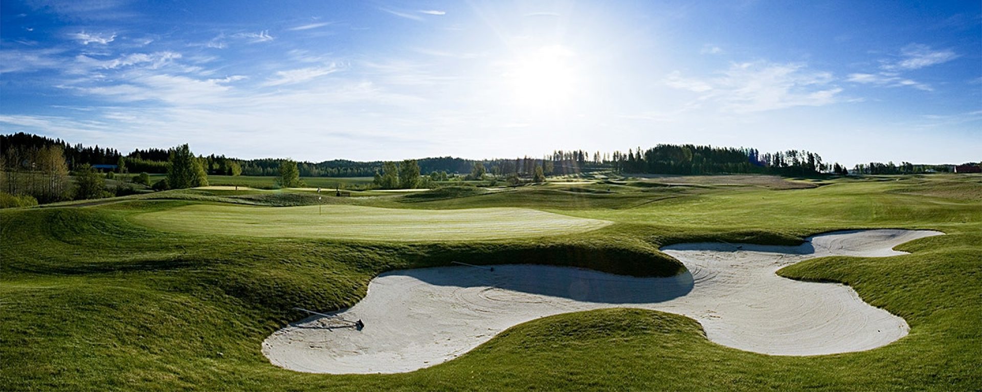 Kaunis golfkenttä, jossa on vihreitä alueita ja hiekkaesteitä auringonpaisteessa.