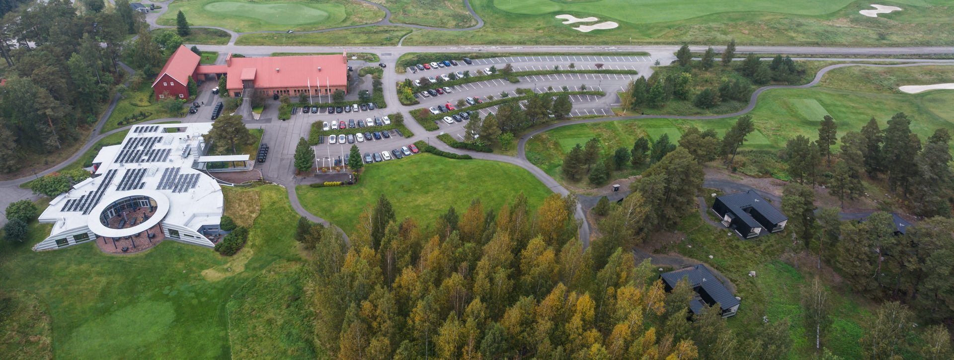 Ilmakuva golfkentästä, jossa on pysäköintialueita ja rakennuksia, ympäröitynä metsäisellä alueella.