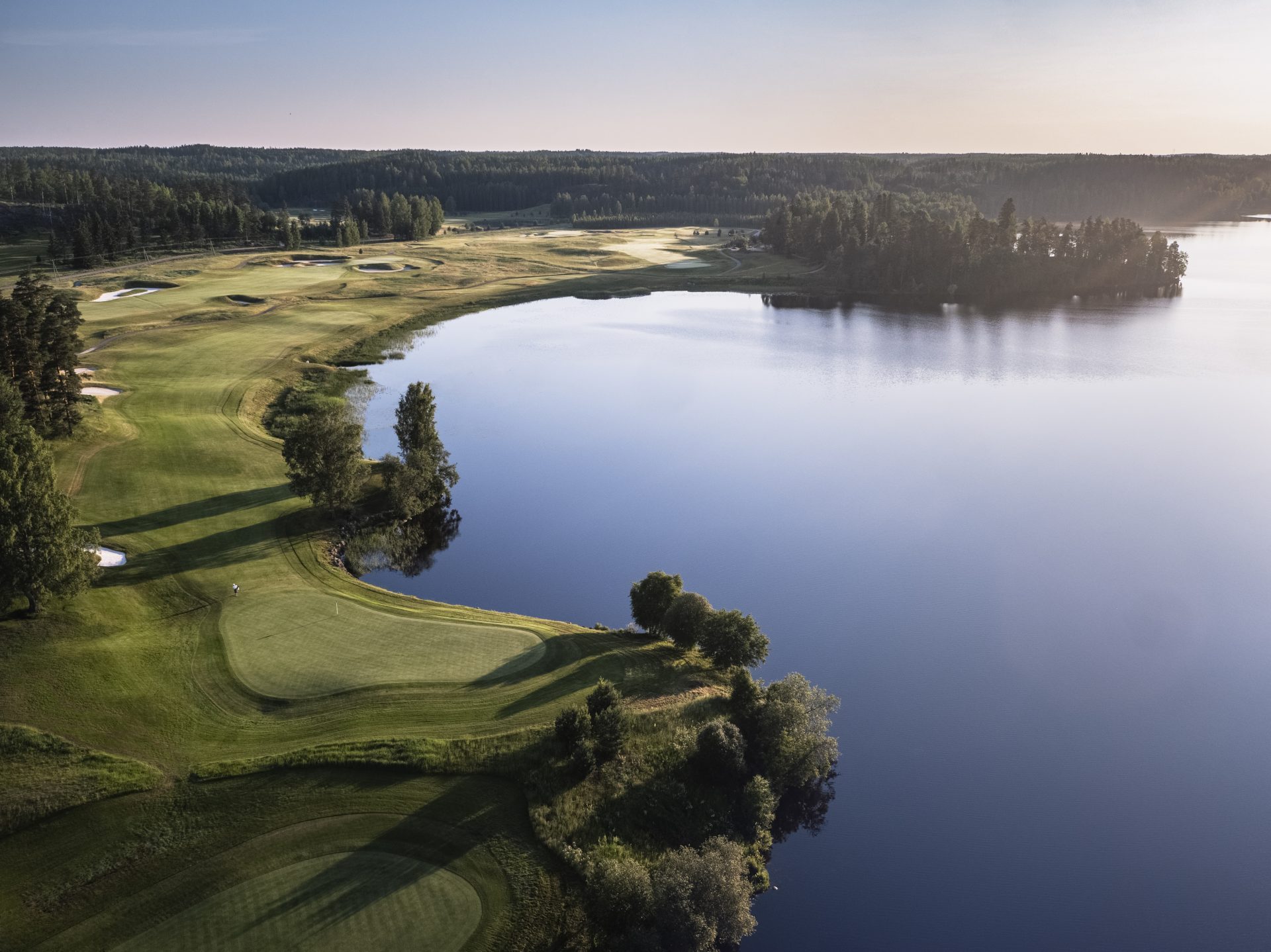 Kaunis golfkenttä, jossa on viheriöitä, metsää ja rauhallinen järvimaisema.
