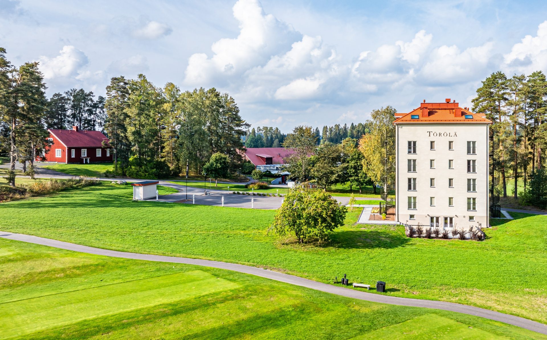 Kauniisti hoidettu maisema, jossa on Törölän rakennus, golf-kentät ja metsää taustalla.