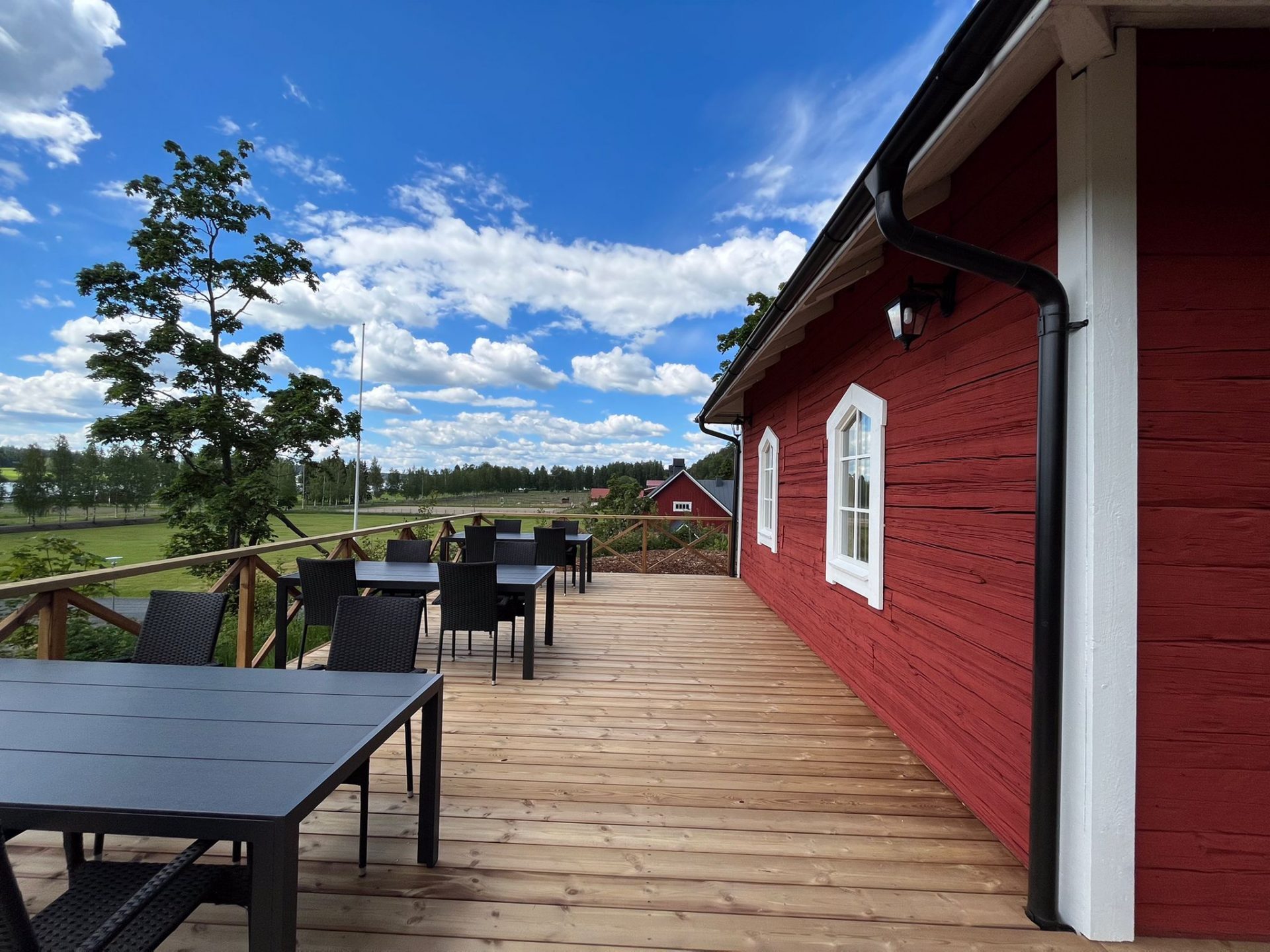 A terrace of a red house featuring black tables and chairs, with beautiful scenery in the background.